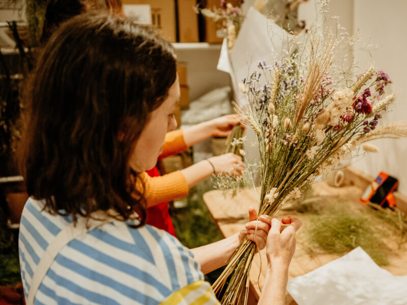A shot from behind of a woman making a floral design with dried foliage.